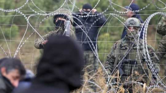 Poľskí policajti a príslušníci pohraničnej stráže hliadkujú pri plote s ostnatým drôtom.