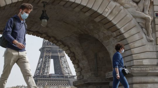 Ľudia s ochrannými rúškami kráčajú cez most Bir-Hakeim v Paríži, v pozadí Eiffelova veža.