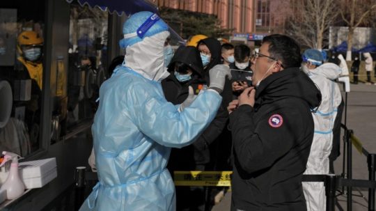 Zdravotník v špeciálnom ochrannom odeve testuje muža na ochorenie COVID-19 v mobilnej testovacej jednotke v Pekingu.