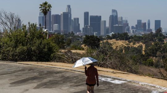 Športovec kráča s dáždnikom s UV-filtrom odrážajúcim slnko počas horúčavy v parku Elysian Park v kalifornskom Los Angeles.