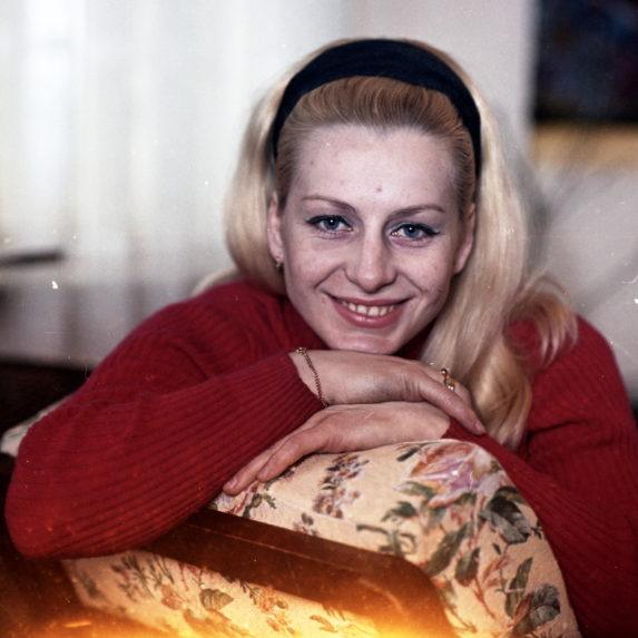 Na snímke gymnastka Věra Čáslavská usmievajúca sa do objektívu, sedí na fotelke v červenom svetri.