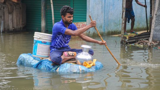 Muž na po domácky vyrobenom člne v zaplavených uliciach Bangladéšu.