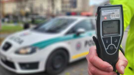 Na snímke policajt drží v ruke tester na alkohol, v pozadí je policajné auto