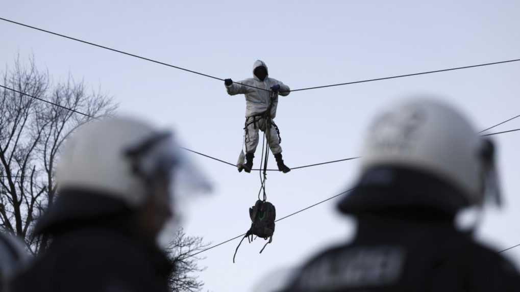 Policajti stoja pred demon&scaron;trantom visiacim na oceľovom lane.