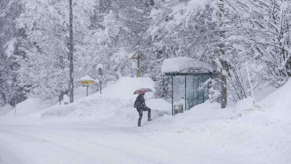 Žena sa snaží dostať k autobusovej zastávke po zasneženej ceste v slovinskom meste Kočevje.