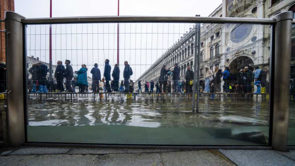 Turisti a obyvatelia kráčajú po móle počas prílivu mora, ktoré dosahuje výšku približne 97 centimetrov, aby prešli po zaplavenom Námestí sv. Marka.