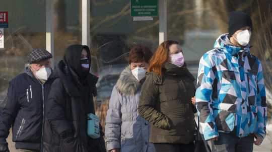 Ľudia na zastávke autobusu s nasadenými rúškami a respirátormi.