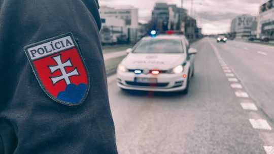 Na snímke je policajt a policajné auto v pozadí.