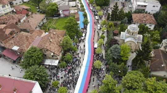 Ľudia držia obrovskú srbskú zástavu počas protestu pred budovou radnice po pondelňajších zrážkach polície s kosovskými Srbmi v obci Zvečan na severe Kosova 31. mája 2023.