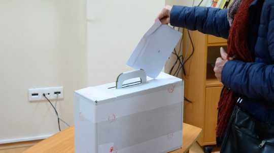Žena vhadzuje obálku do volebnej urny.