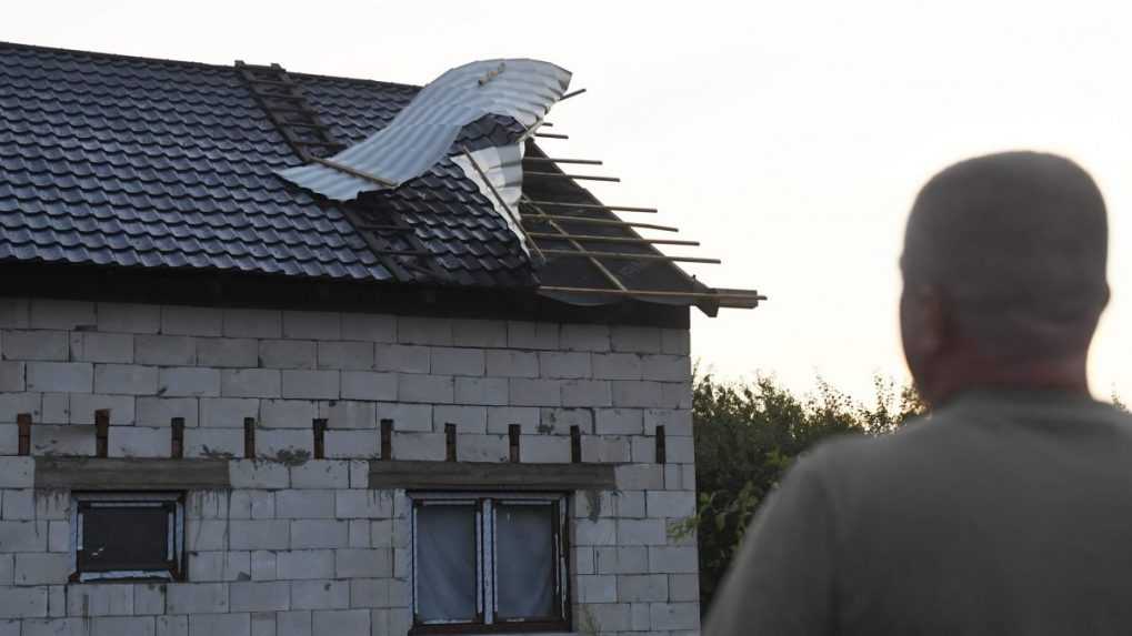 Na snímke muž hľadí na dom, ktorého strechu poškodil vietor