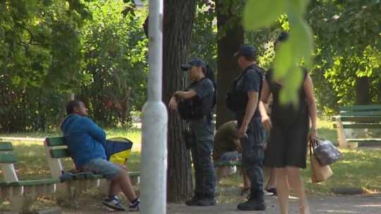 Na snímke bezdomovec sedí na lavičke a rozprávajú sa s ním policajti.