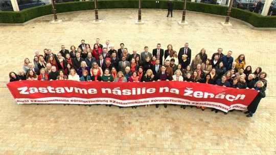 Na snímke skupina ľudí držiaca plagát s nápisom: Zastavme násilie na ženách.