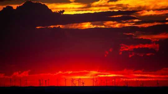 Červené nebo a siluety veterných turbín veternej elektrárne.