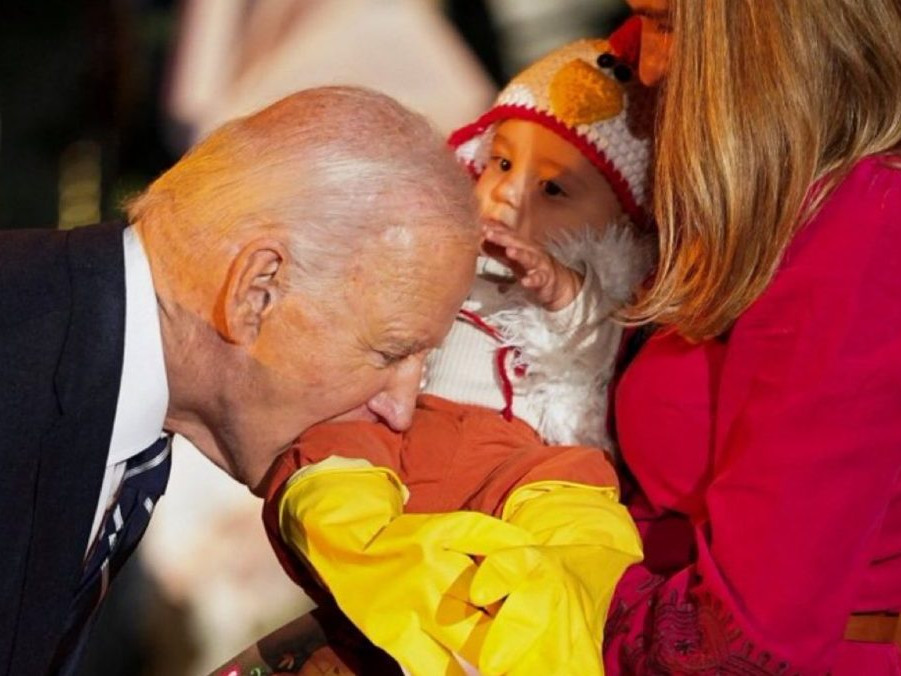 Prezident USA Joe Biden predstiera, že hryzie dieťa v kostýme kurčaťa.