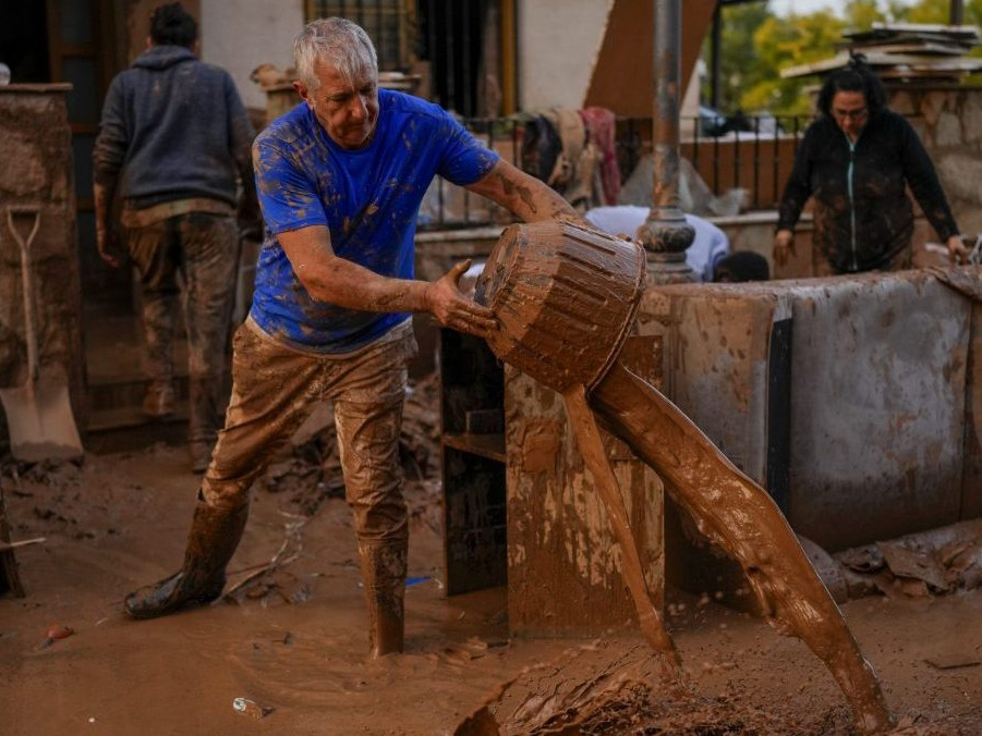muž vylieva vodu na ulicu po povodniach v Španielsku.