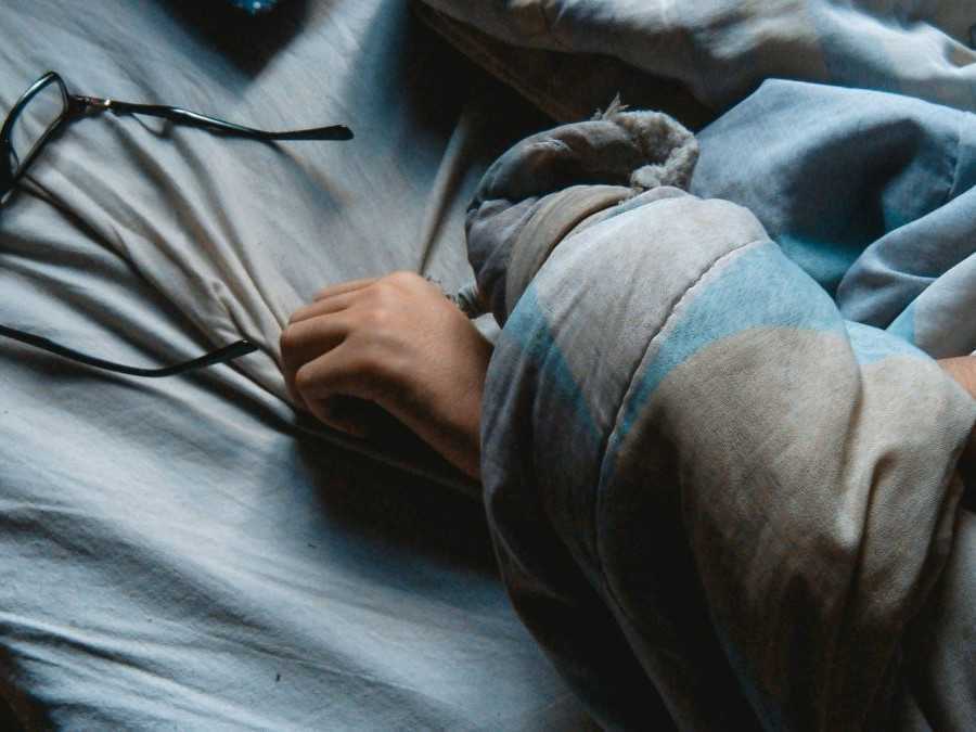 Osoba v posteli spod paplóna siaha po dioptrických okuliaroch.