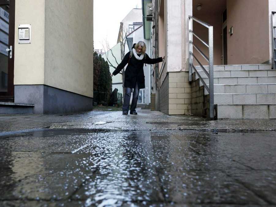 Žena sa snaží prejsť po zľadovatenom chodníku pri bytovom dome.