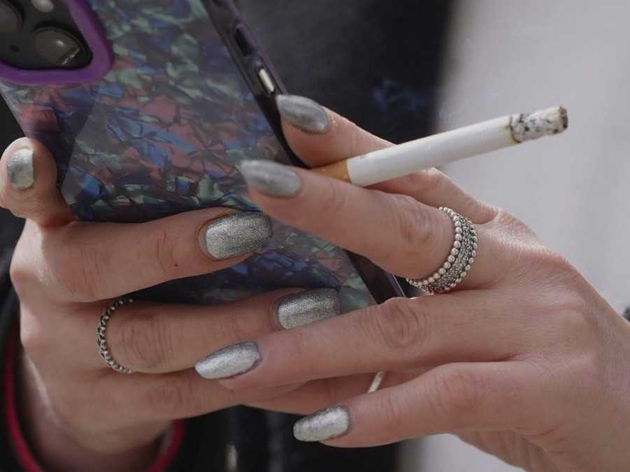 Na snímke žena držiaca mobil a zapálenú cigaretu.