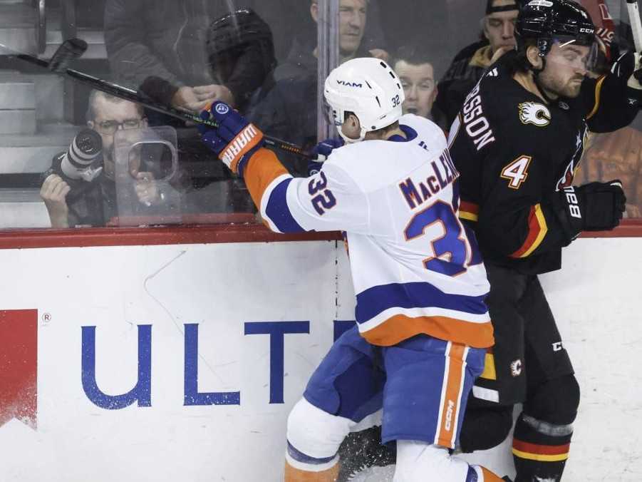 Zľava Kyle MacLean z New York Islanders v súboji o puk s Rasmusom Anderssonom z Calgary Flames.