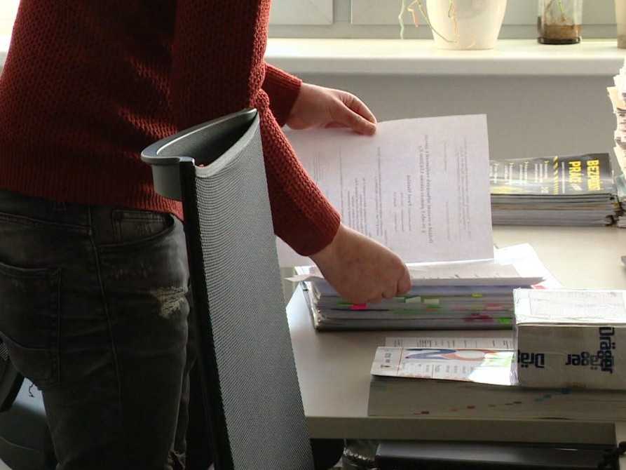 Muž listuje v kôpke papierov na stole.