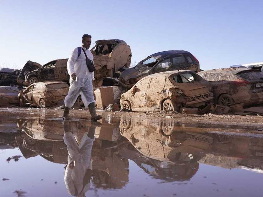 Muž prechádza okolo nahromadených áut po záplavách, ktoré si vyžiadali stovky mŕtvych v regióne Valencia.