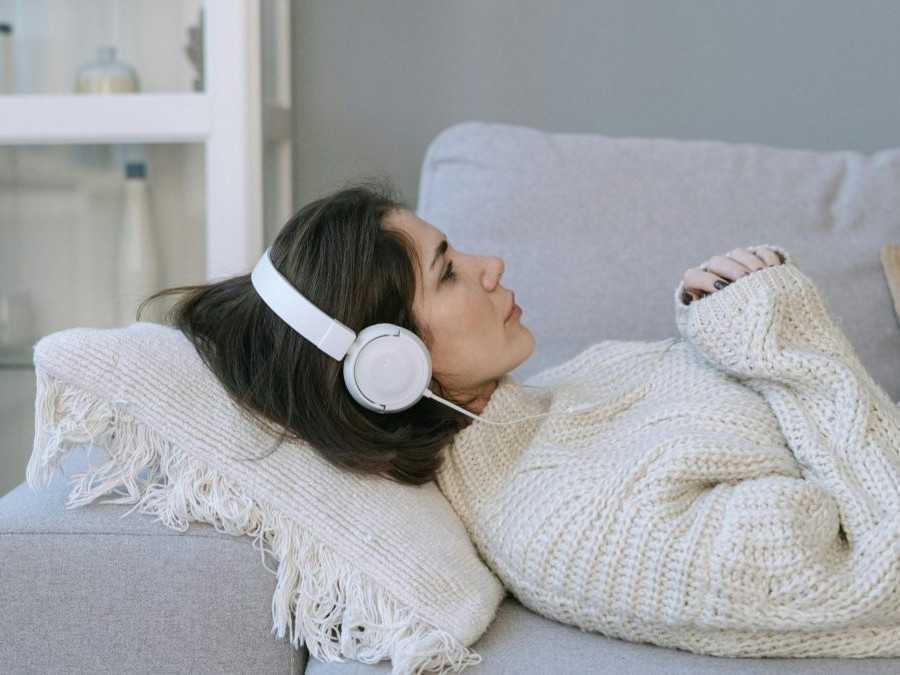 Žena leží na gauči počúvajúc hudbu cez slúchadlá.