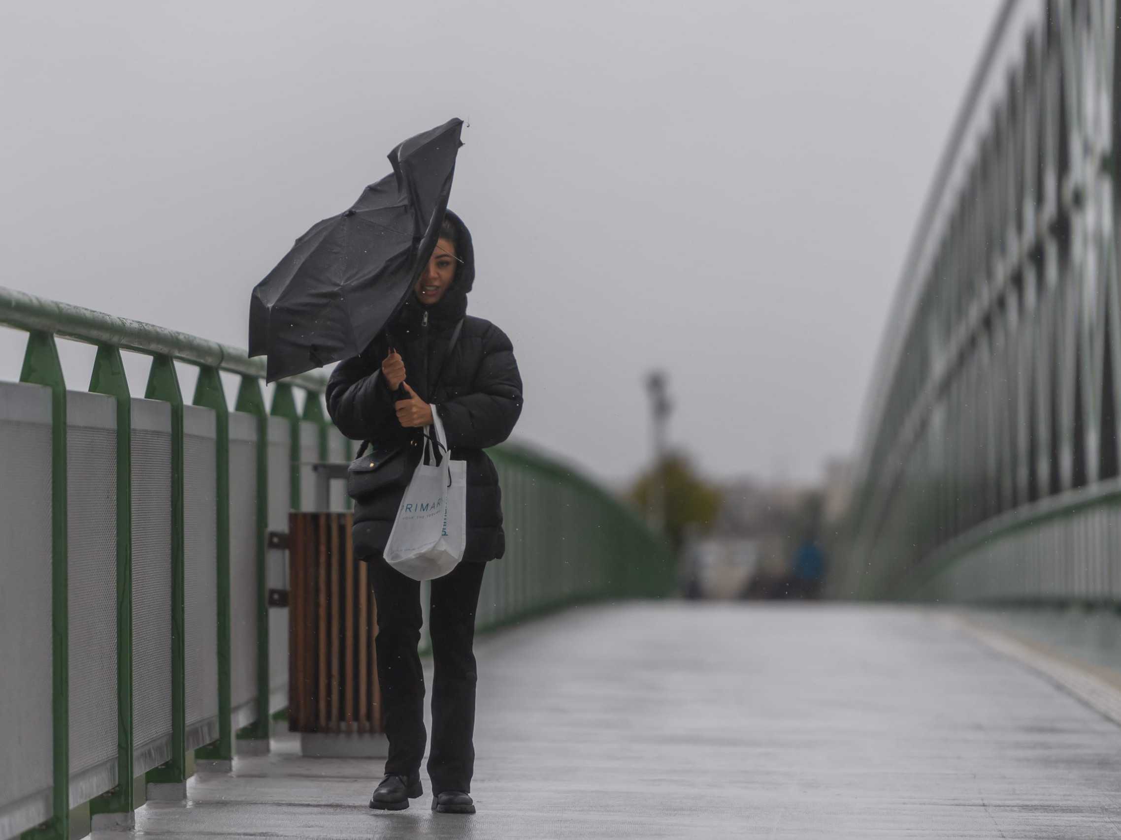 Žena z dáždnikom kráča počas vetra po Starom moste v Bratislave.