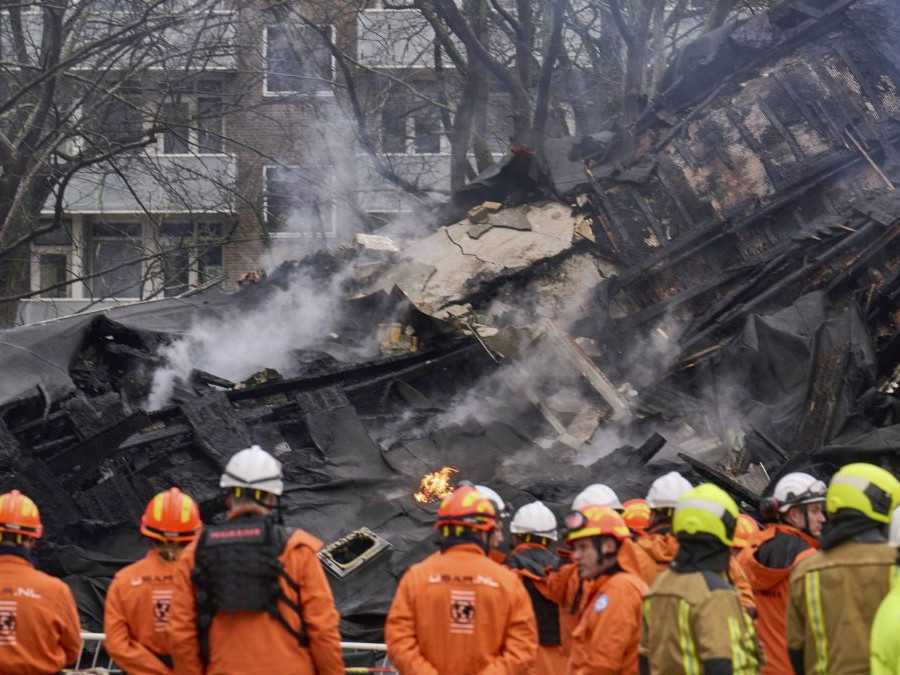 Hasiči stoja pri zničenej budove na mieste výbuchu.