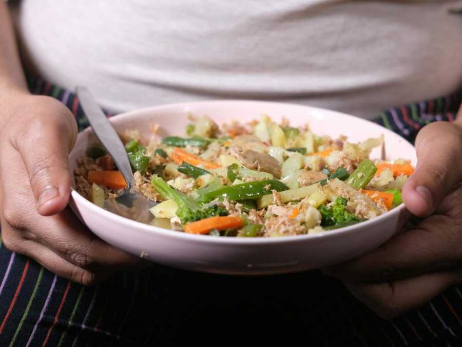 Na snímke obézna osoba drží tanier so šalátom.