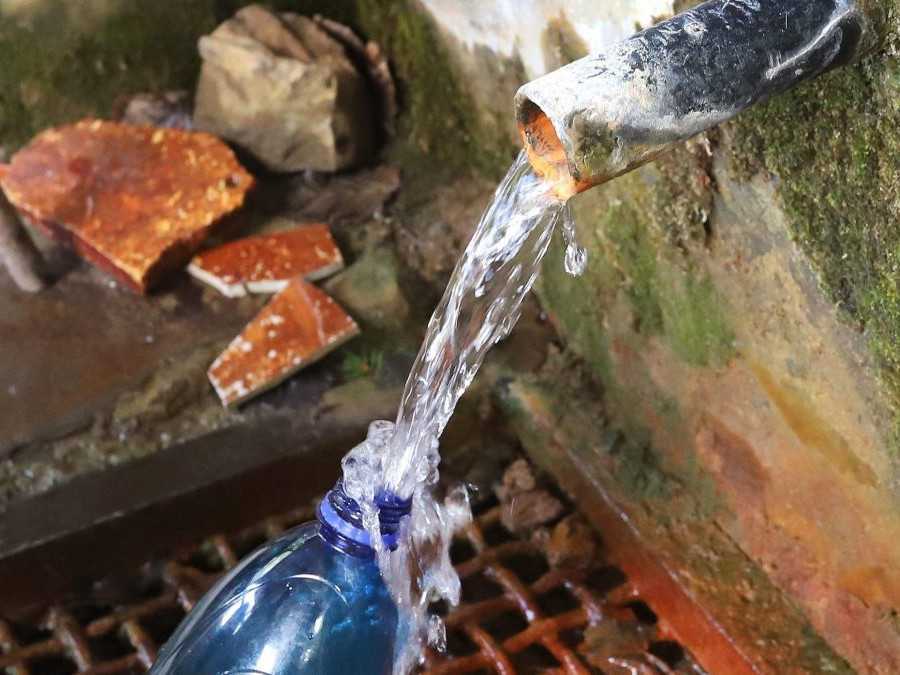 Osoba naberá vodu do fľaše z prameňa.