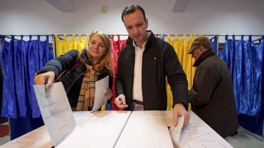 Muž a žena vhadzujú hlasovací lístok do volebnej urny