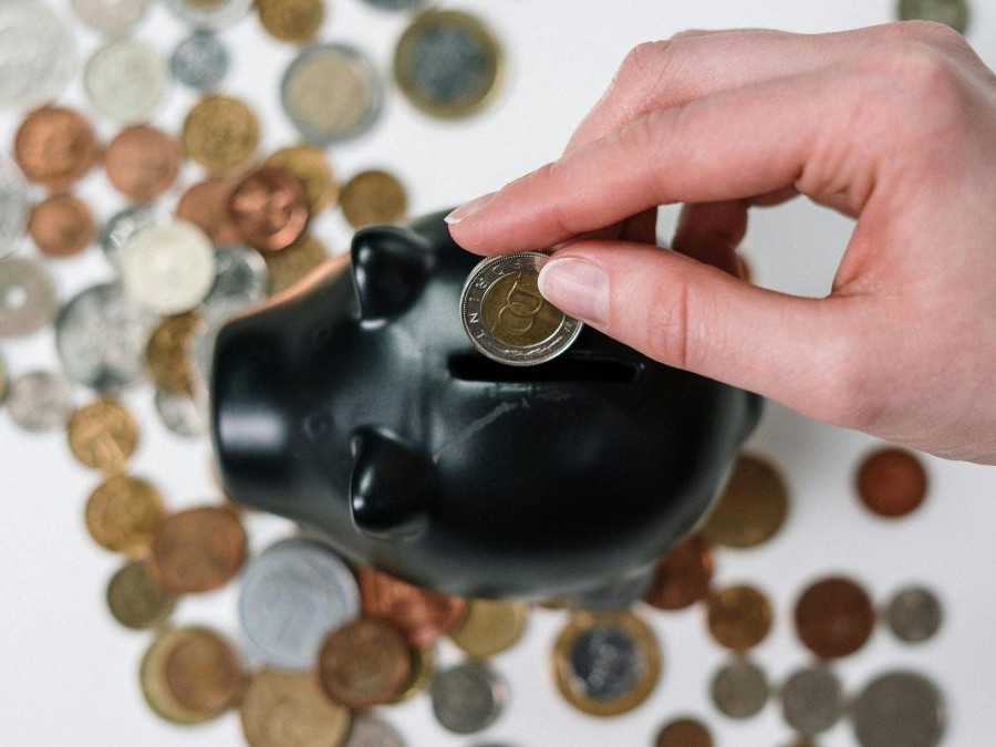 Osoba vhadzuje mincu do hlinenej šporiacej nádoby v tvare prasaťa.