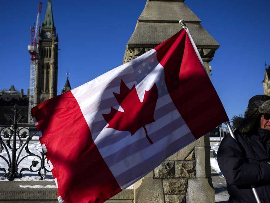 Protestujúci drží vlajky Kanady a Spojených štátov pred budovou parlamentu v Ottawe.