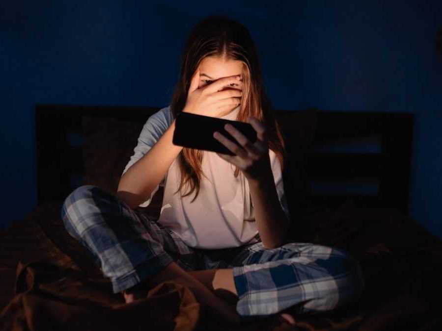 Na snímka tínedžerka pozerá na jasnú obrazovku telefónu v tmavej miestnosti.