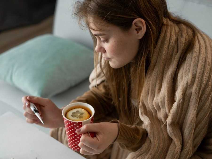 chorá žena si meria teplotu s čajom v ruke