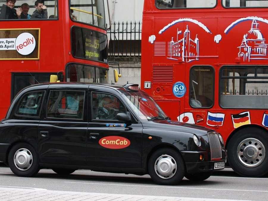 Na snímke je čierny taxík v Londýne pri dvoch červených dvojposchodových autobusoch.