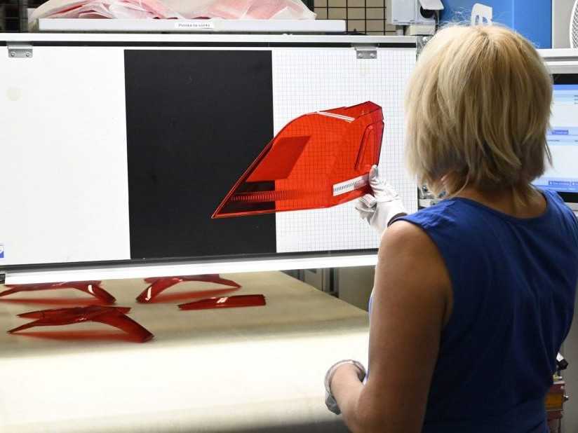 Zamestnankyňa kotroluje výrobok zo vstrekolisu vo výrobnej hale.