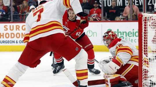 Jesperi Kotkaniemi (Carolina Hurricanes) naháňa puk pred brankárom Calgary Flames Dustinom Wolfom počas druhej tretiny hokejového zápasu NHL.