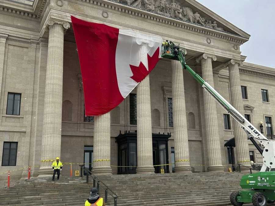 Na ilustračnej sníme robotníci inštalujú vlajku Kanady na legislatívnu budovu vo Winnipegu.