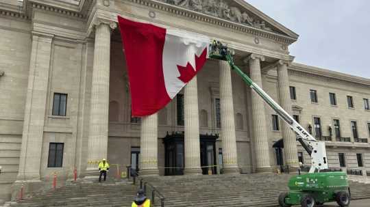 Na ilustračnej sníme robotníci inštalujú vlajku Kanady na legislatívnu budovu vo Winnipegu.