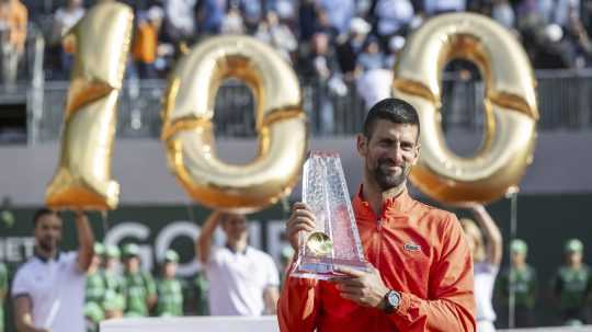 Novak Djokovič, za ním balóny v tvare čísla 100.