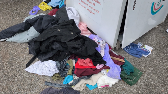 Rozhádzané oblečenie pri kontajneri na textil.