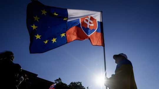 Na ilustračnej snímke osoba drží vlajky Slovenska a EÚ.