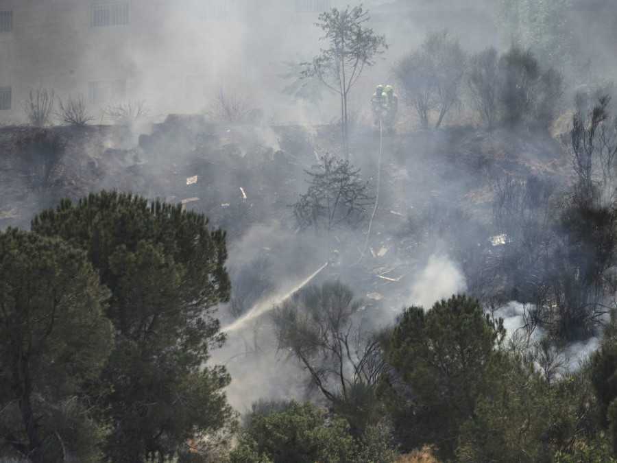 Hasiči zasahujú pri lesnom požiari v Izraeli. Z lesu stúpa hustý dym.