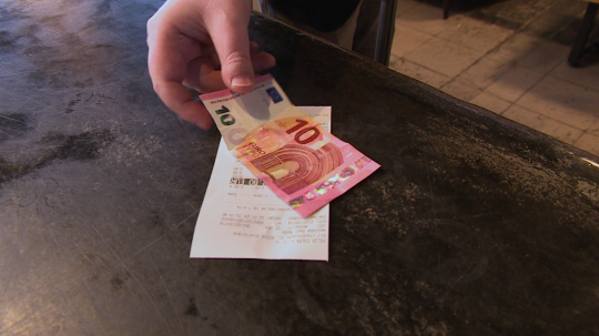 Osoba platí v hotovosti, na snímke desaťeurová bankovka a bloček na pulte.