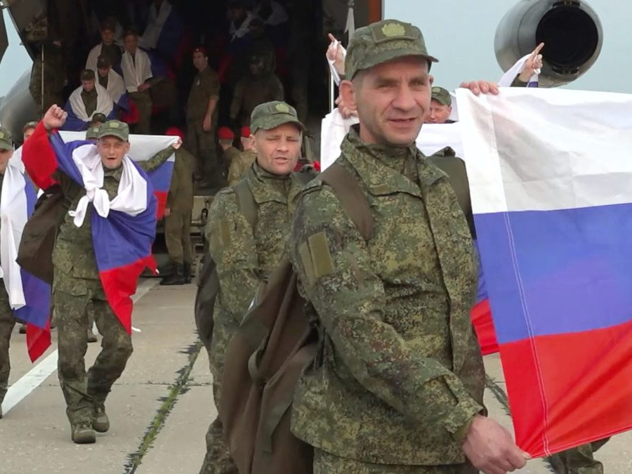 Ruskí vojaci počas výmeny väzňov stoja pri lietadle, v rukách držia ruské vlajky.