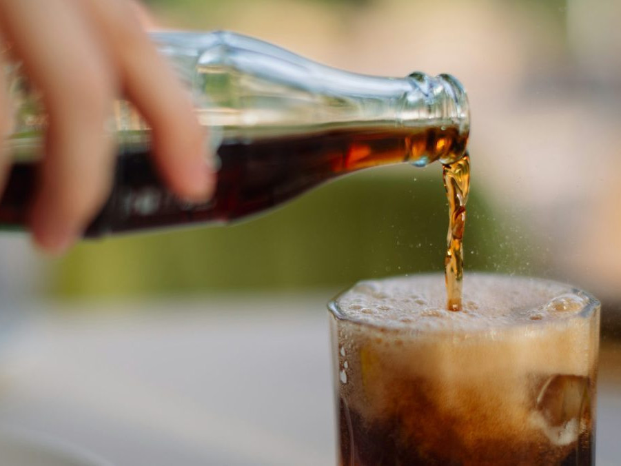 Na snímke človek prelieva sladký nápoj z fľaše do pohára.