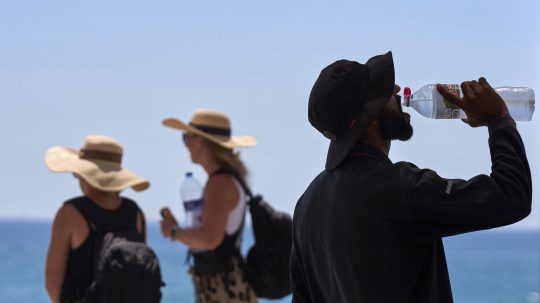 Na archívnej snímke z 2. júla 2025 turista pije vodu počas hrorúčav na pláži v Barcelone.