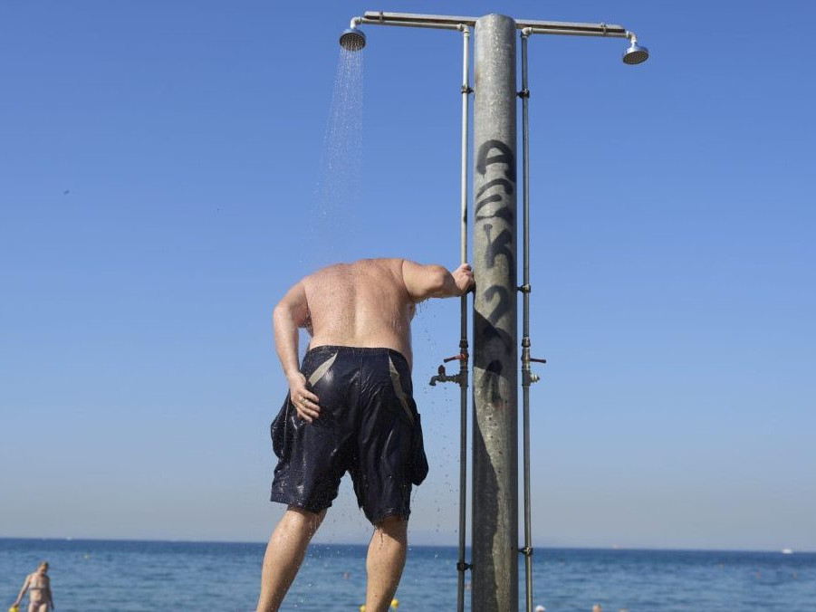 Muž sa osviežuje pod sprchou na pláži Alimos pri Aténach.